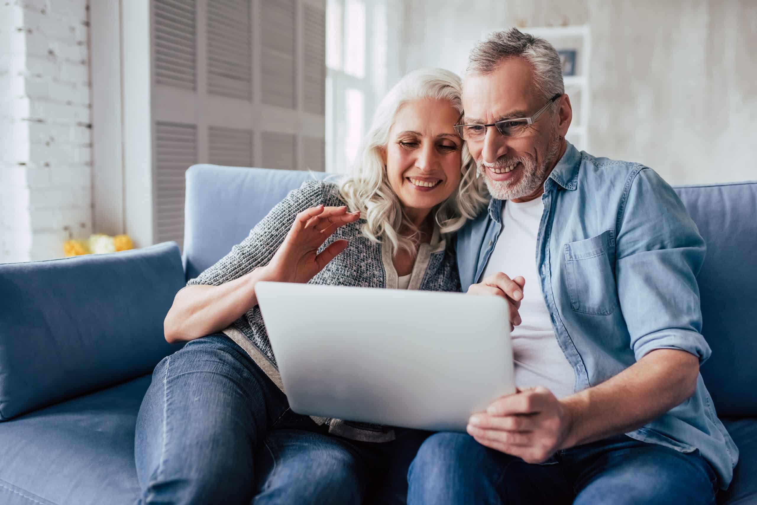Love lives forever! Senior couple at home. Handsome old man and attractive old woman are spending time together. Sitting on a sofa with laptop.